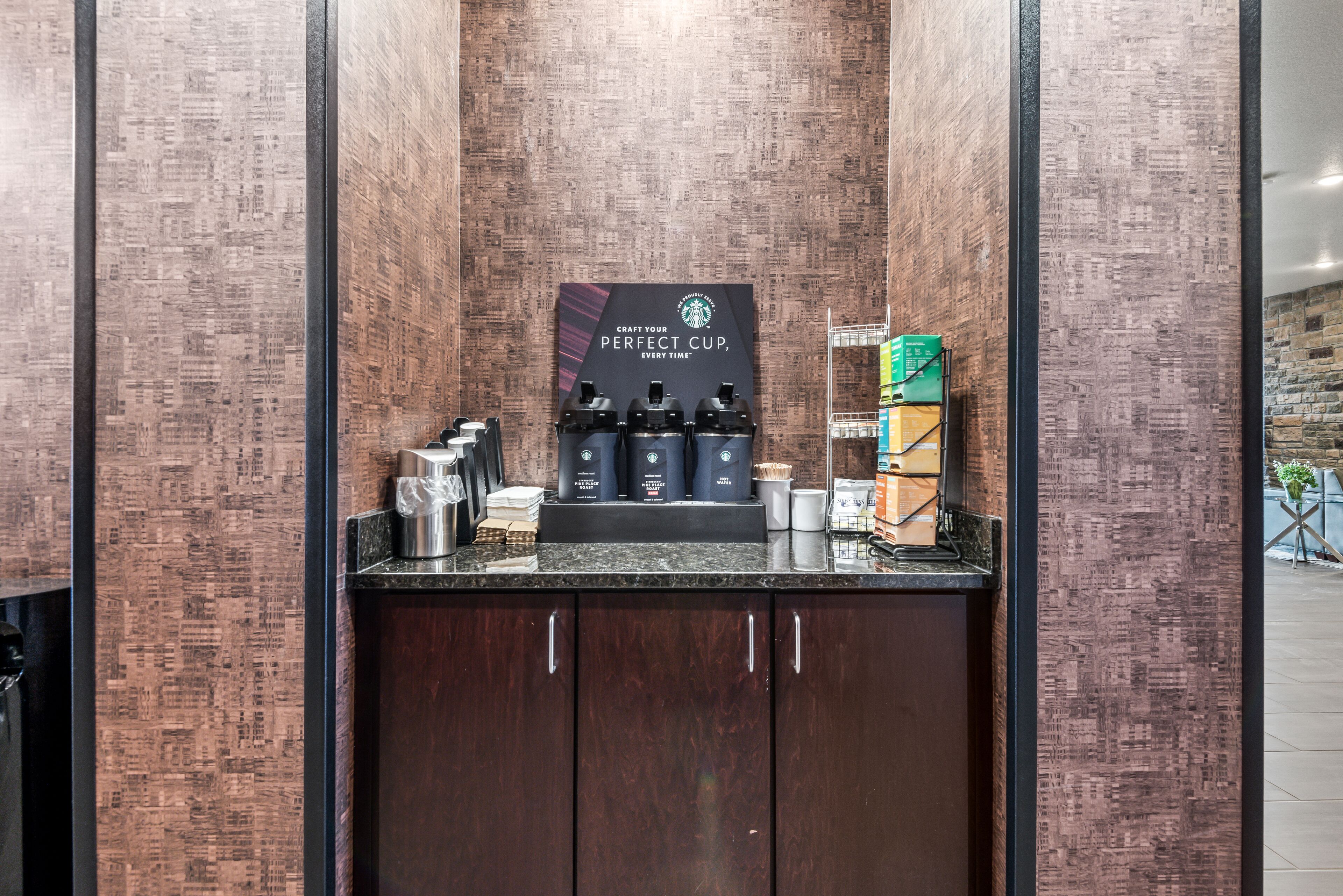 A coffee station with a Starbucks sign, a coffee machine, and various coffee cups and containers.