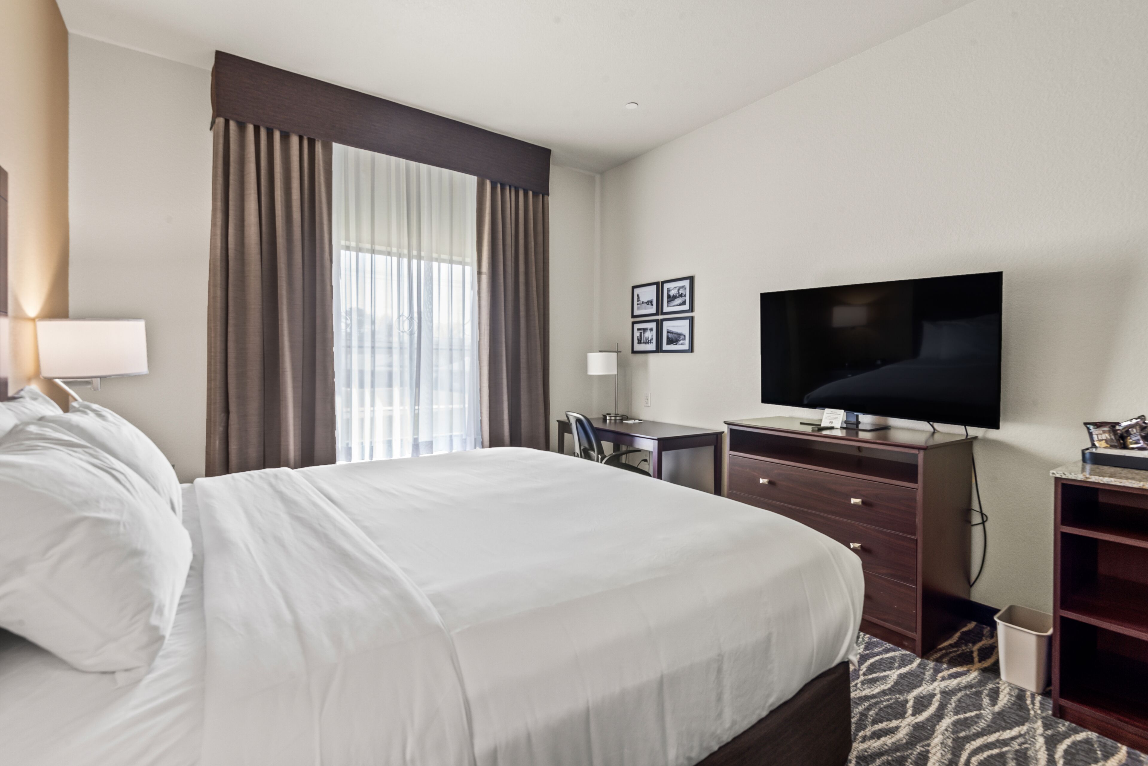 Una habitación de hotel con una cama grande, un escritorio, un televisor y una ventana con cortinas.