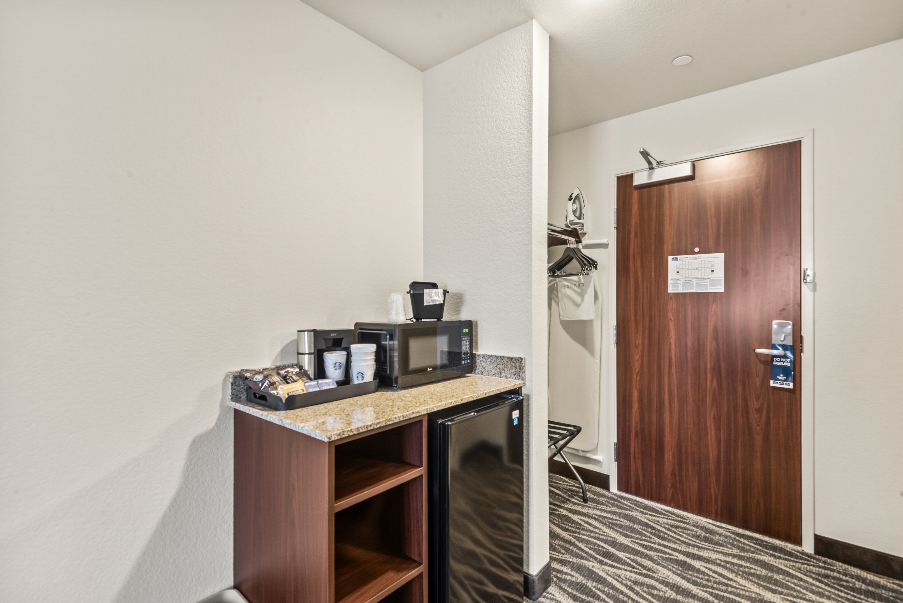 Habitación de hotel compacta con kitchenette que incluye refrigerador, microondas, cafetera y un lavamanos pequeño.