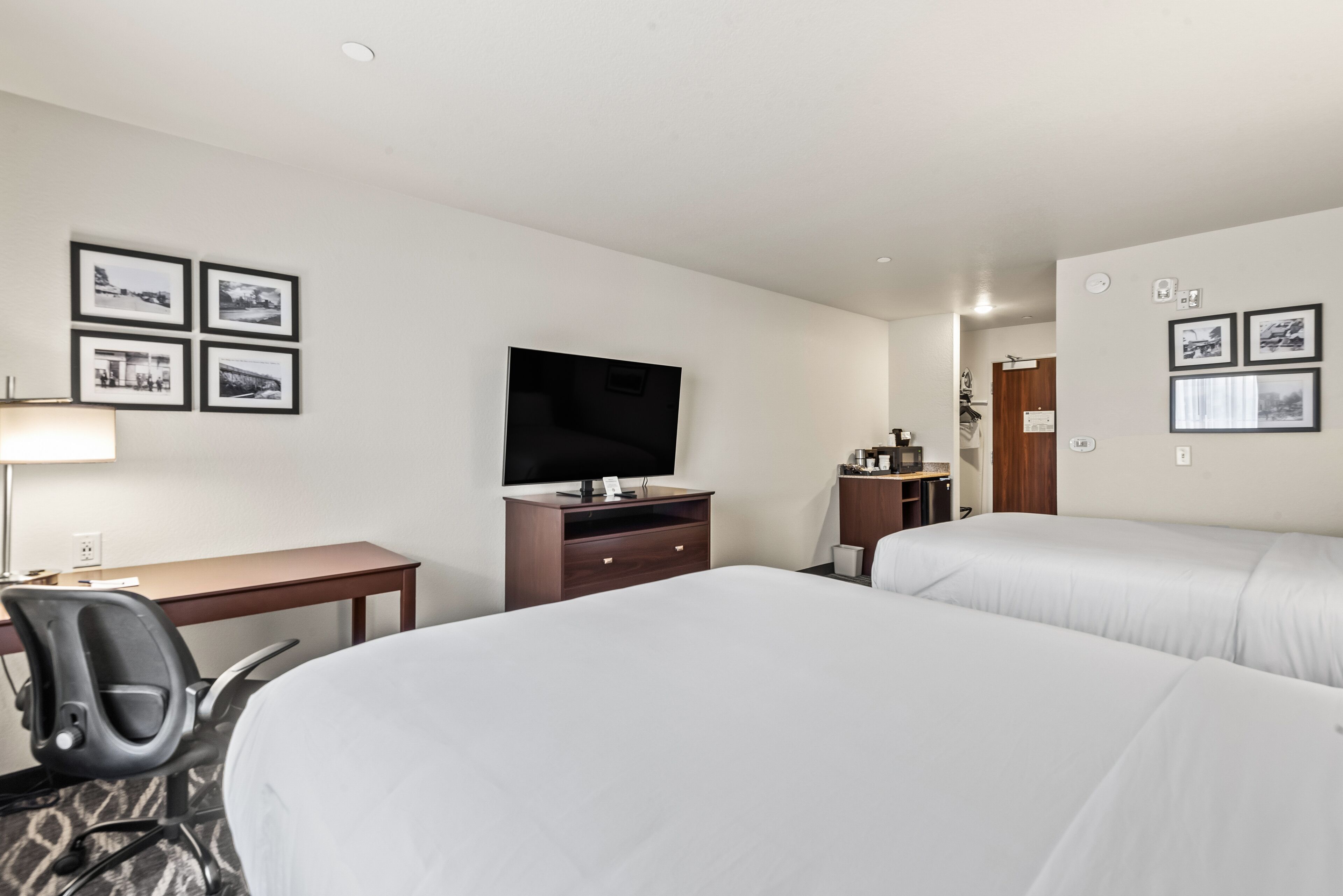 Ein Hotelzimmer mit zwei Betten, einem Schreibtisch, einem Sessel, einem Fernseher und gerahmten Bildern an den Wänden.