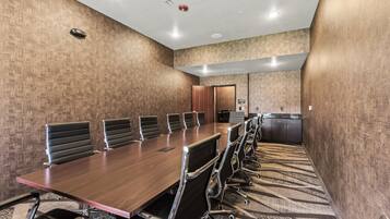 A conference room with a long table, multiple chairs, and a kitchenette area.