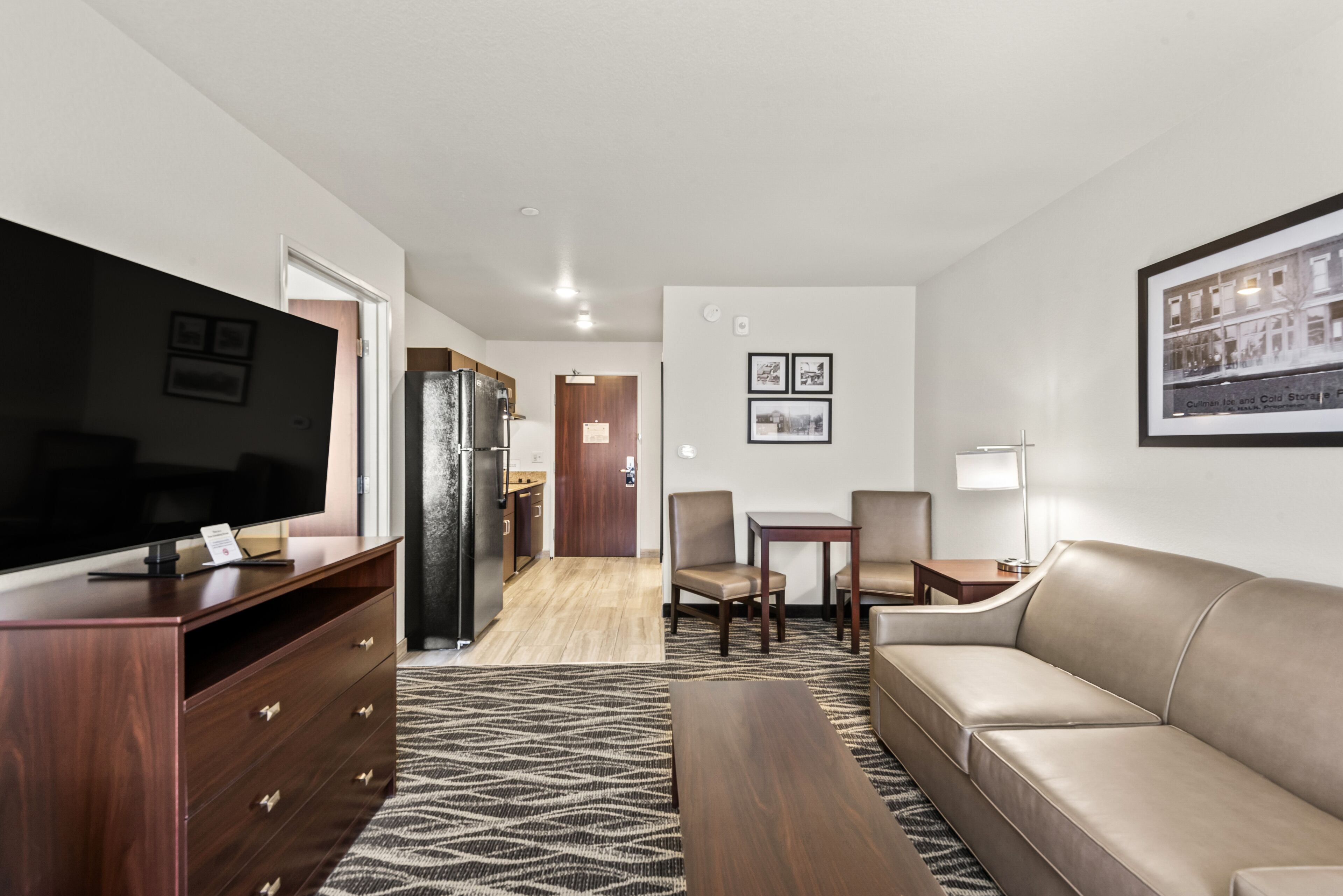 Habitació d'hotel moderna amb televisió de pantalla plana, mobles de fusta, zona de menjador i finestra gran.