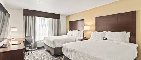 A hotel room with two beds, a desk, a chair, and a large window with curtains.