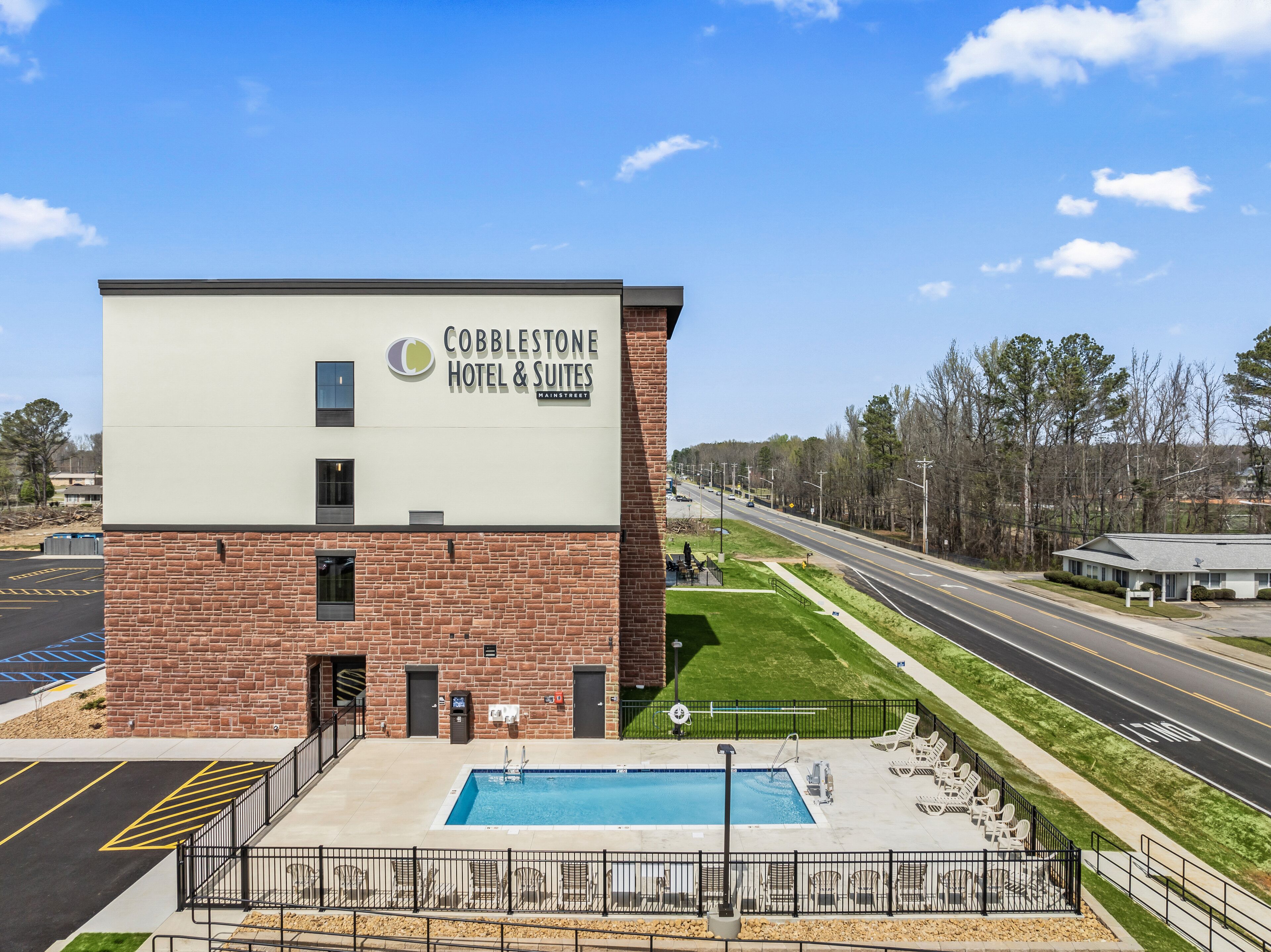 A Cobblestone Hotel & Suites building with a swimming pool and outdoor seating area.