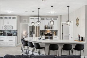 Una cocina moderna con armarios blancos, electrodomésticos de acero inoxidable y taburetes negros.