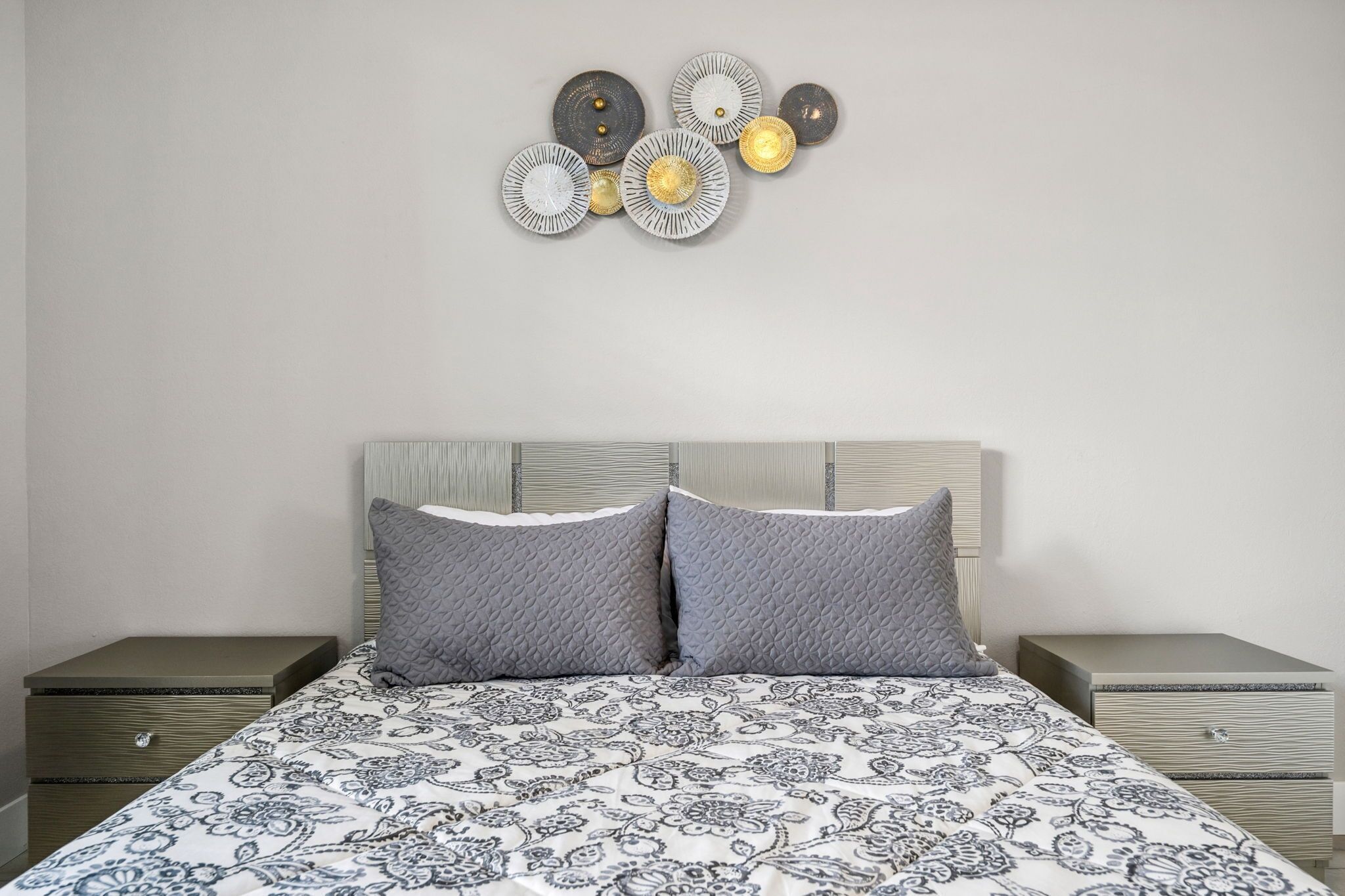 Une chambre à coucher comprenant un lit, deux tables de chevet et un élément décoratif fixé au mur.