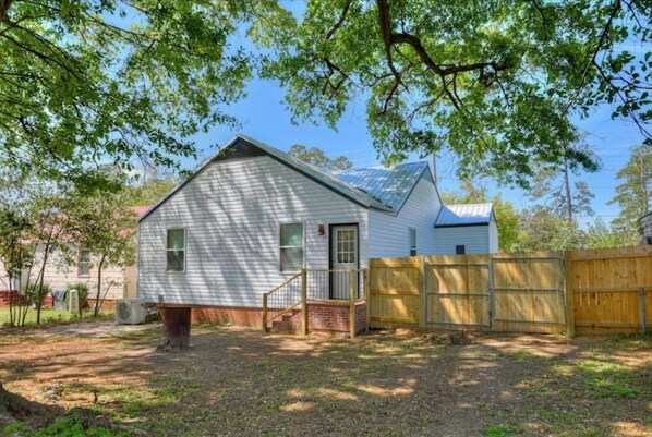 Situated in a serene backyard, this charming house features a front door, small porch, and a grassy yard with a shaded area.