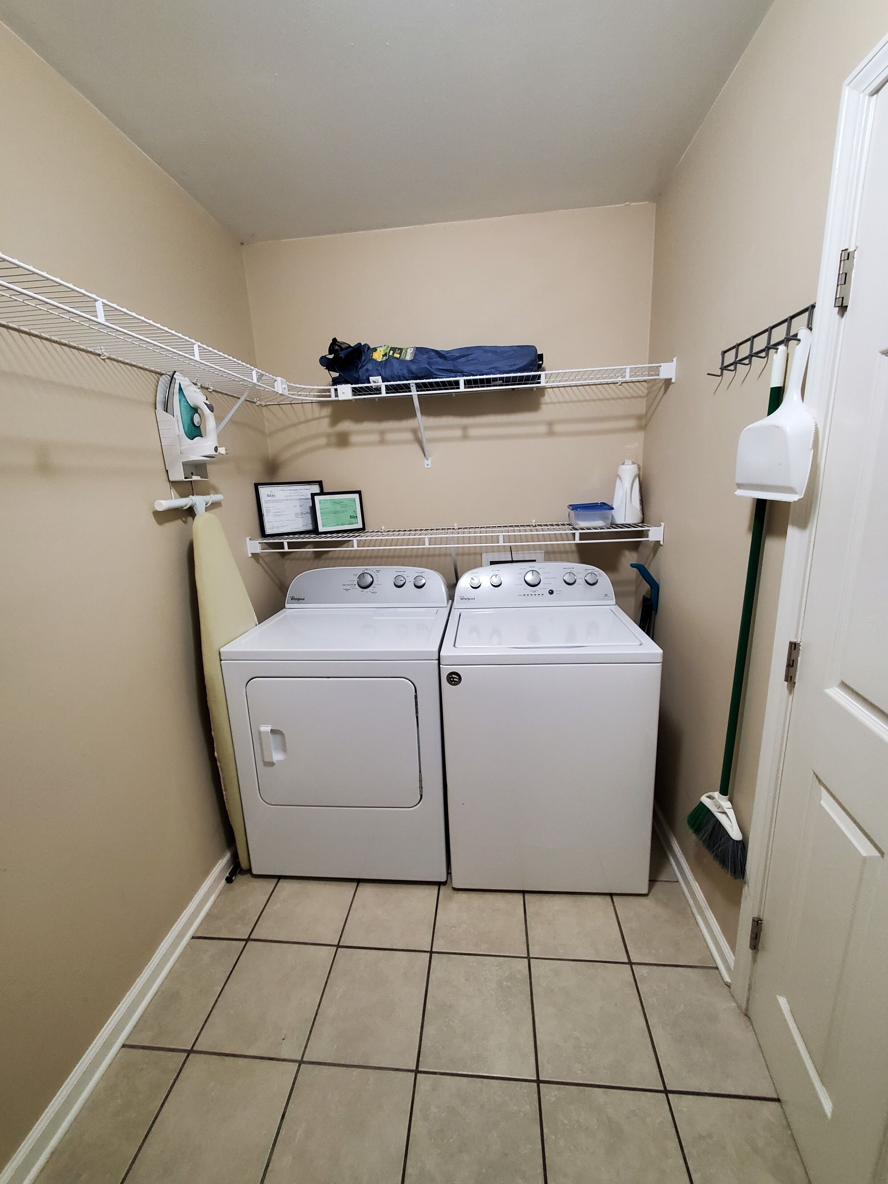 A laundry room with two front-loading washing machines, a drying rack, and a broom.