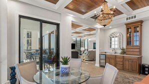 Un salón amplio con una mesa de vidrio, sillas blancas, una planta en maceta y techo de madera.