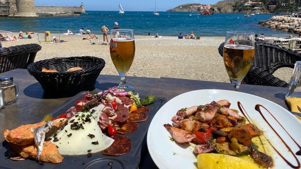 Ein Esstisch am Meer mit Meeresfrüchten, zwei Biergläsern und Blick auf Strand und See.