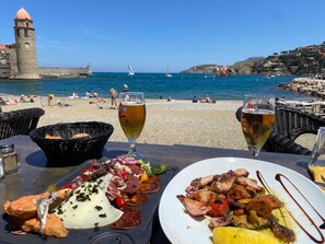 Mesa junto al mar con platos de mariscos, dos vasos de cerveza y vistas a la playa y al océano.