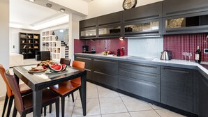 A modern kitchen with dark cabinetry, a red backsplash, and a dining area with a table and chairs. - Villa with Private Pool & Jacuzzi Naxos (Naxos)