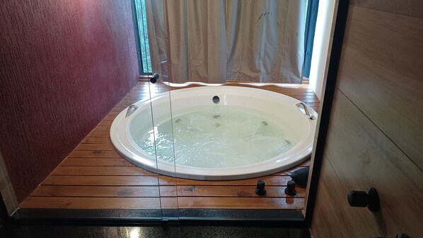 A hot tub in a room with wooden flooring and a red wall.