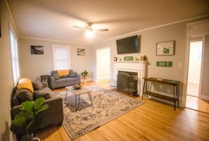 Een woonkamer met een open haard, een bank, een salontafel en een televisie aan de muur.
