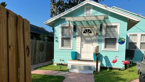 Une maison turquoise avec un porche à l’avant, une clôture en bois et un chemin de briques menant à la porte.