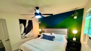 Ein Schlafzimmer mit einem Bett, einem Deckenventilator, einer Wandleuchte und einem gerahmten Bild.