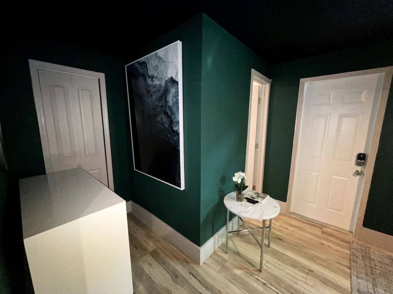 Un couloir aux murs verts, aux portes blanches et à la table surmontée d’un plateau de marbre, agrémentée d’un vase de fleurs.