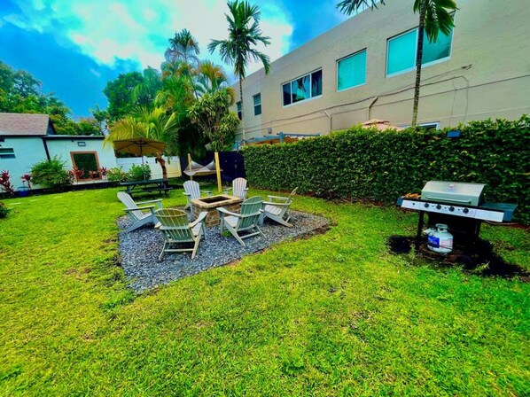 A backyard with a grill, outdoor seating, and a house in the background.