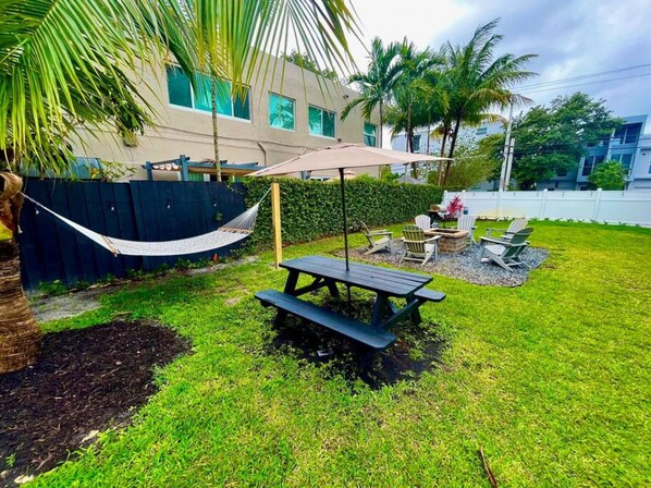 Un jardin avec une table de pique-nique, des chaises, un hamac et une piscine.