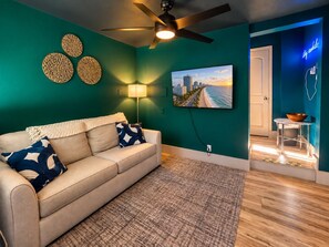 A living room with a beige sofa, patterned rug, wall art, and a ceiling fan.