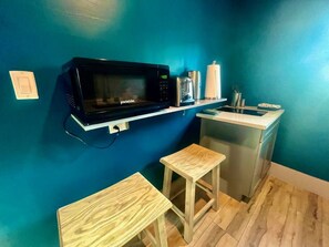 A compact kitchenette with a microwave, a small sink, and two stools.