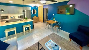 A modern kitchen with a central island, dining area with chairs, and a ceiling fan.
