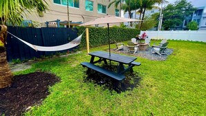 A backyard with a picnic table and chairs, a hammock, and a poolside area with umbrellas.