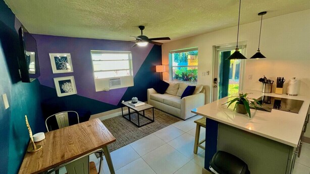 A modern living room with a sofa, coffee table, and dining table. There is a kitchen area with a sink and countertop.