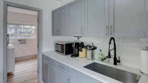 A kitchen with grey cabinets, a microwave, a sink, and a window. - Bahama Mama 2/1 in Las Olas & Holiday Park with Hot Tub! (Fort Lauderdale)