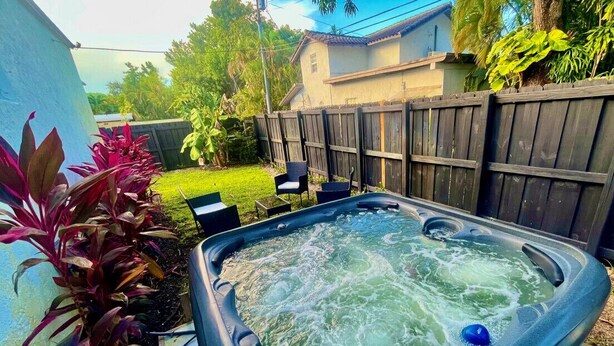 A hot tub in a backyard with a wooden fence, a lawn, and some plants. - Bahama Mama 2/1 in Las Olas & Holiday Park with Hot Tub! (Fort Lauderdale)