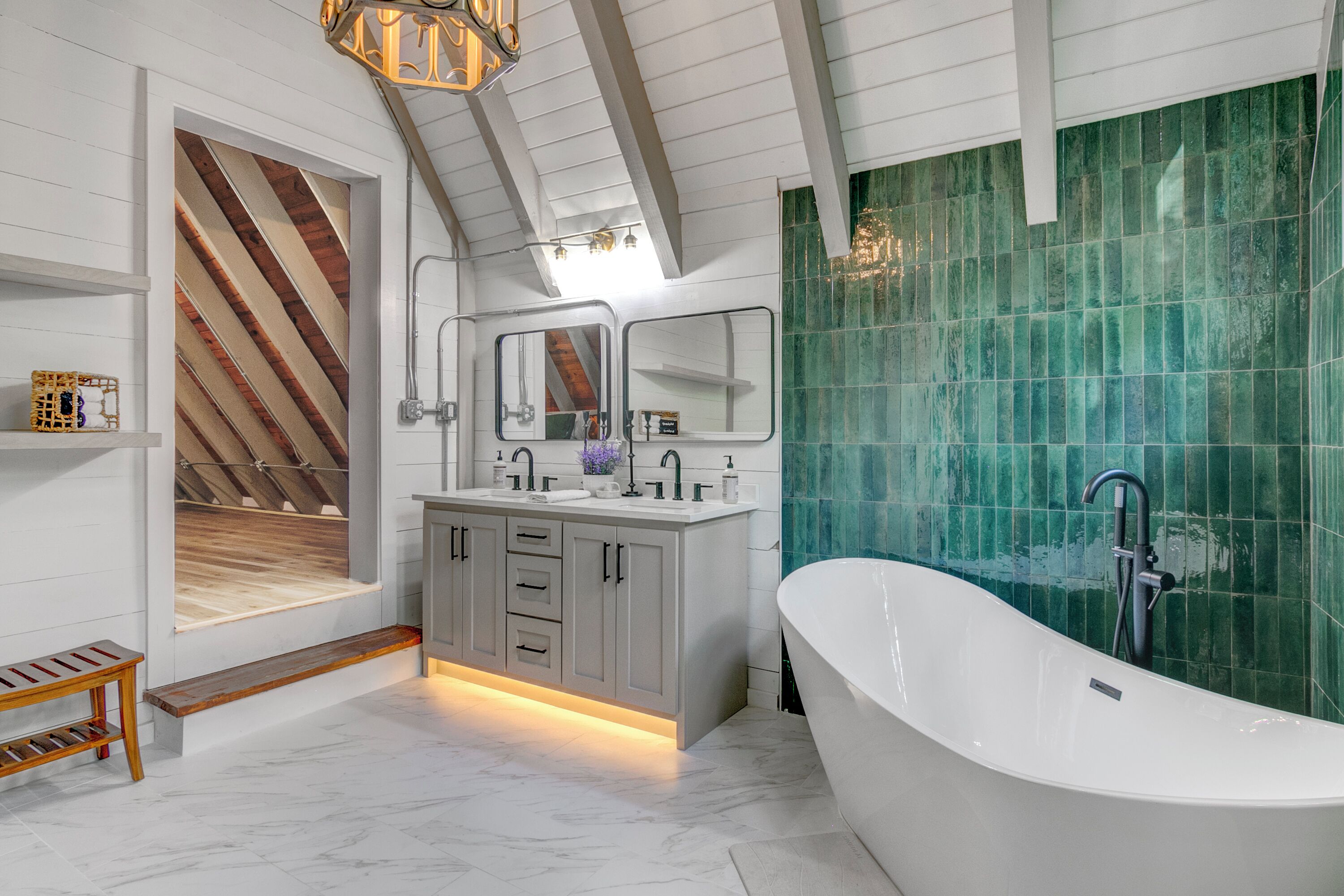 A modern bathroom with a freestanding bathtub, a vanity with a mirror, and a green-tiled wall.