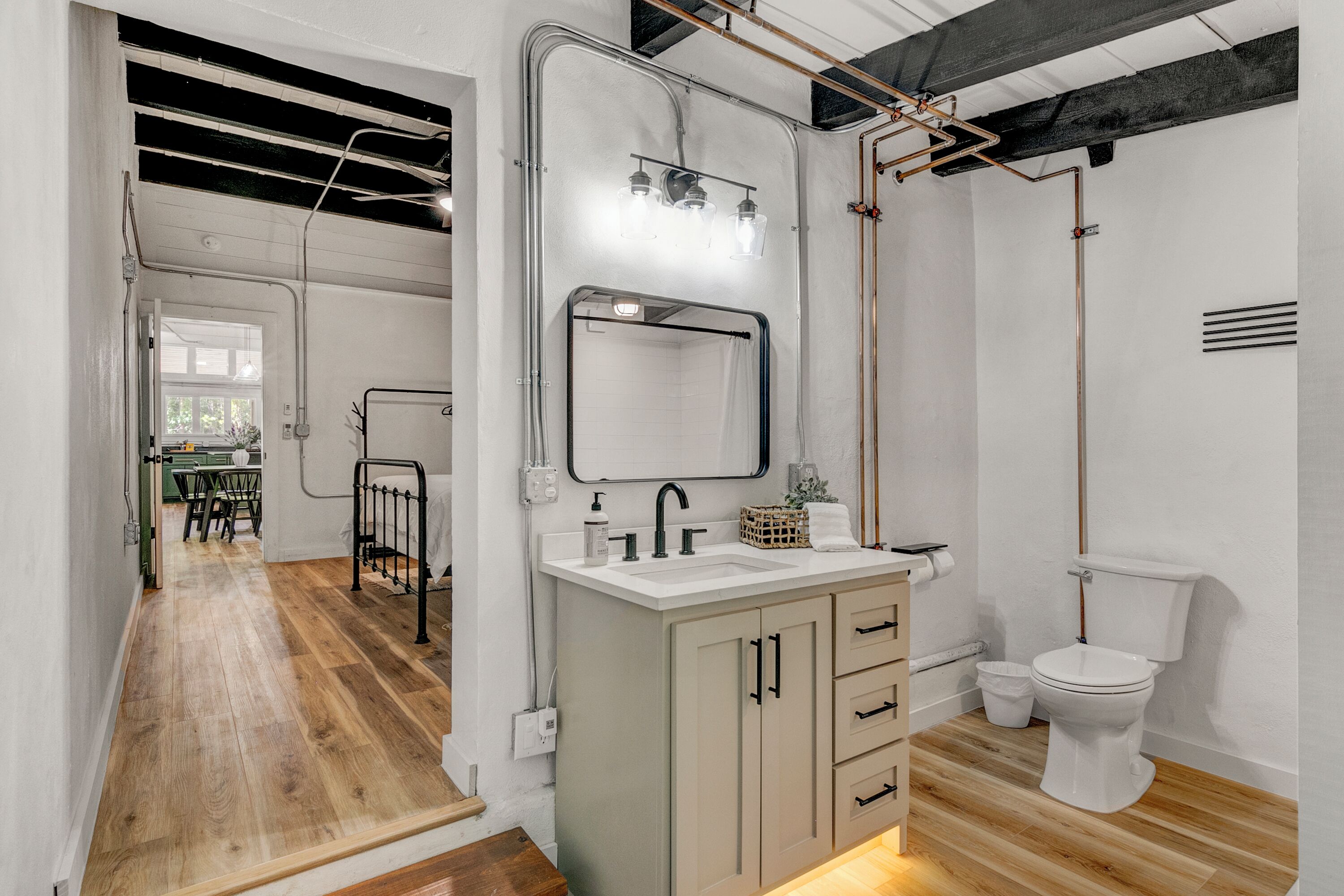 A modern bathroom with a wooden floor, a sink with a mirror, and a toilet.