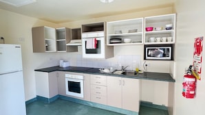 A compact kitchen with a built-in oven, a microwave, and a sink. There are cabinets and shelves above the counter, and a fire extinguisher mounted on the wall.