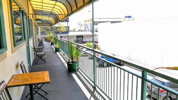 A balcony with a curved roof, outdoor seating, potted plants, and a view of the street below.