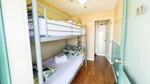 A dormitory room with bunk beds, a wooden floor, and a door with a number.