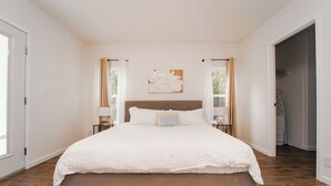 Een ruime slaapkamer met een groot bed, een nachtkastje, een aan de muur bevestigd kunstwerk en uitzicht op het landschap door een raam.