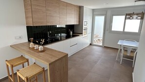A modern kitchen with wooden cabinets, a black countertop, and two wicker stools. - NEW flat 50 meters from the sea !!! (Lo Pagán)