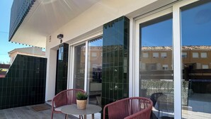 A modern outdoor patio with two wicker chairs and a small table, large sliding glass doors, and a view of the surrounding buildings. - NEW flat 50 meters from the sea !!! (Lo Pagán)