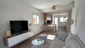 A modern living room with a large flat-screen TV, a grey sectional sofa, a small white coffee table, and a kitchen in the background. - NEW flat 50 meters from the sea !!! (Lo Pagán)