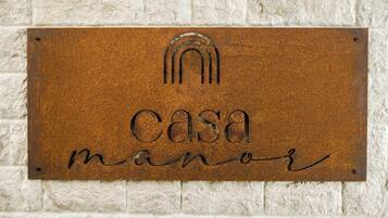 Une plaque métallique portant l’inscription « Casa manor » est fixée à un mur à texture.
