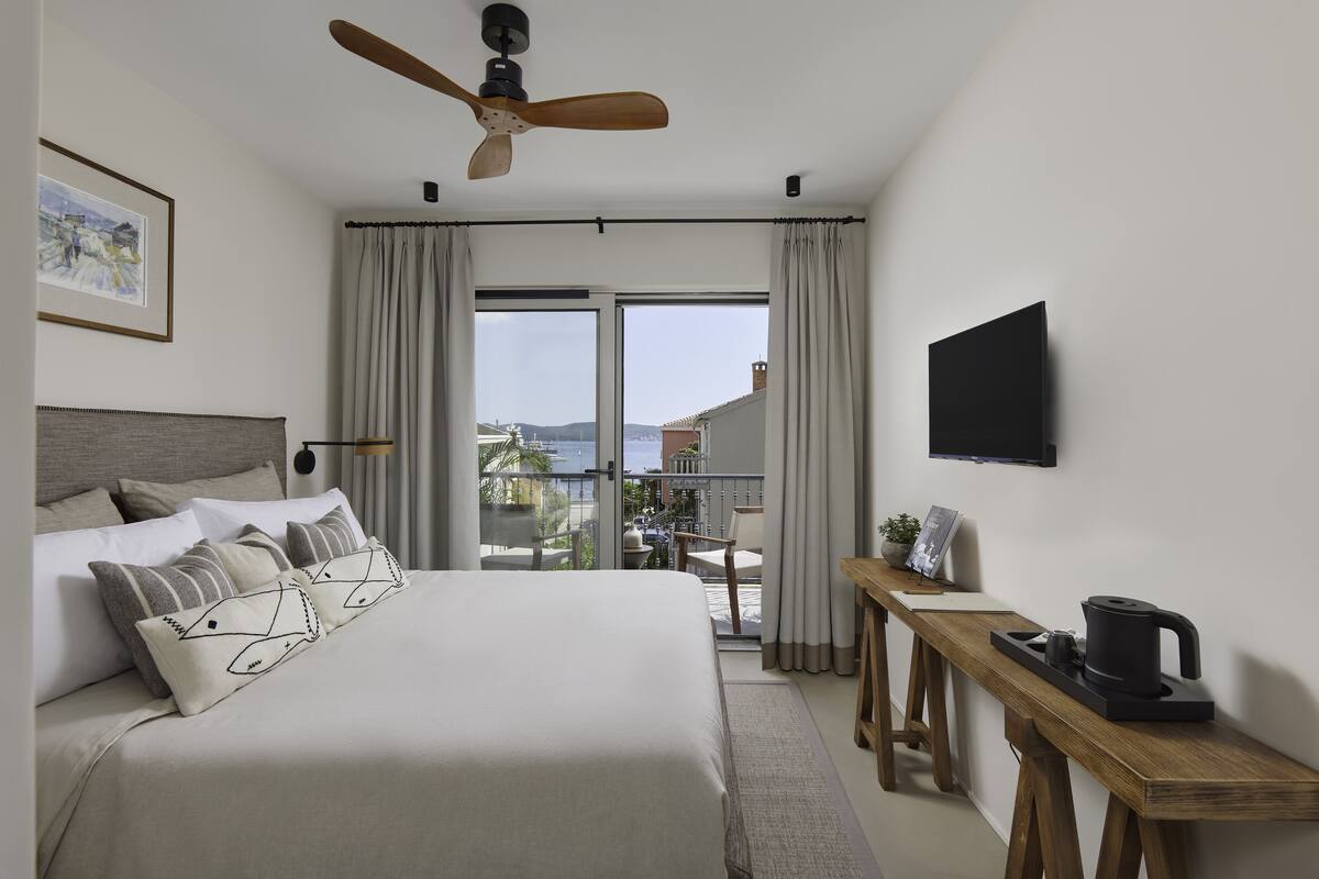 A hotel room with a bed, a desk with a coffee maker, a TV, and a balcony with a view.