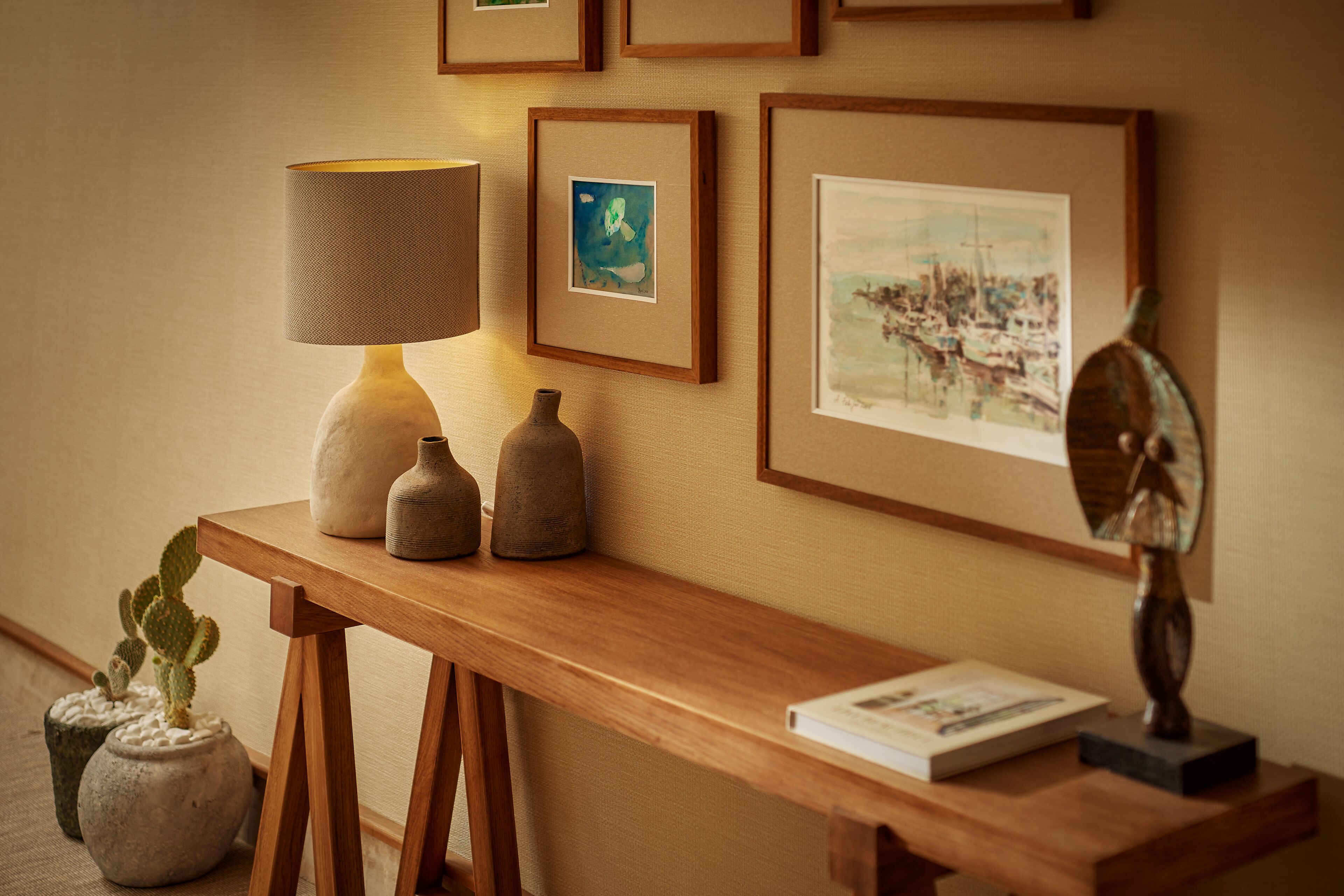Una consola de madera con una lámpara, obras de arte enmarcadas y objetos decorativos.
