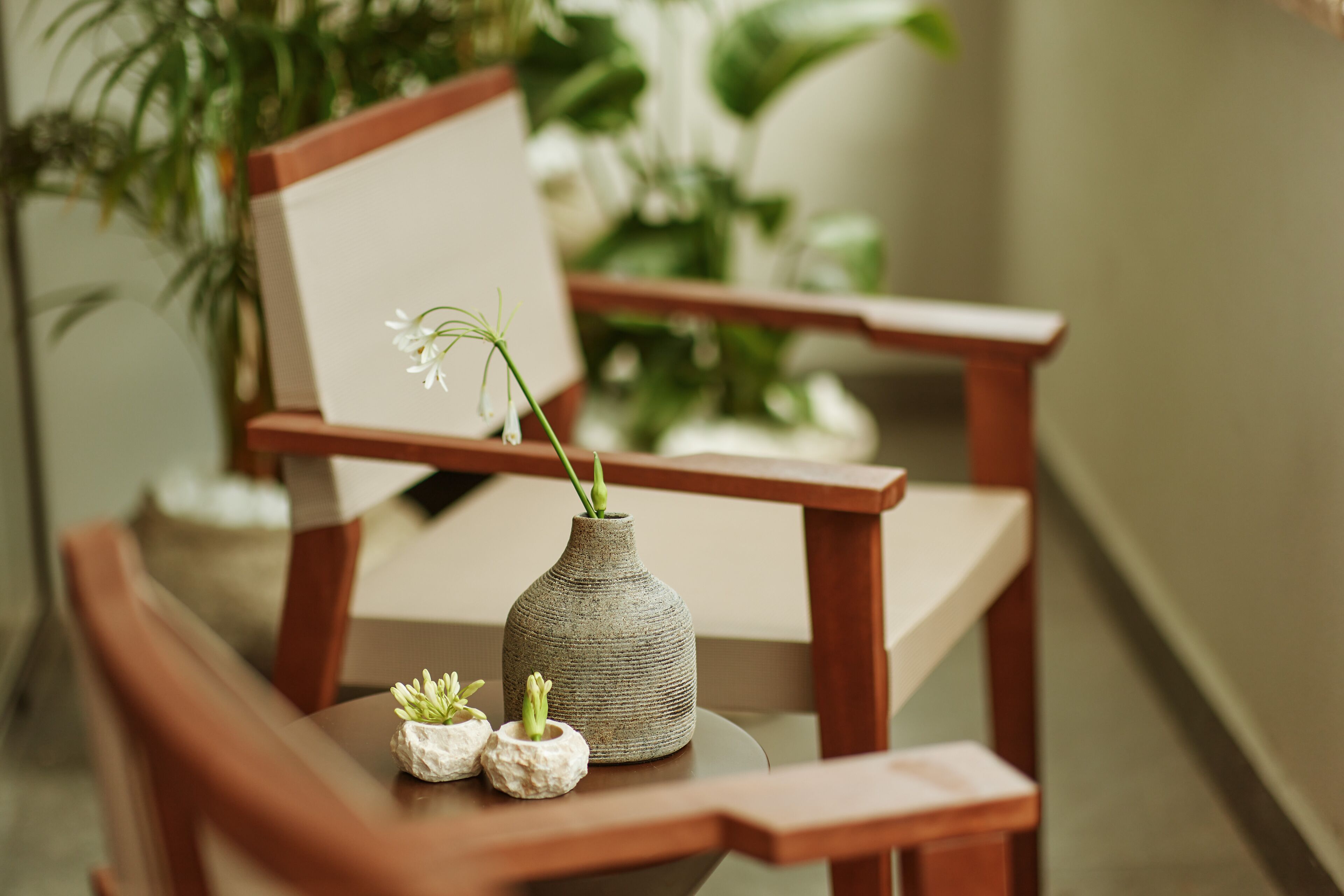 A wooden chair with a small table, a vase with a plant, and a framed picture.