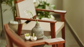 A wooden chair with a small table, a vase with a plant, and a framed picture.
