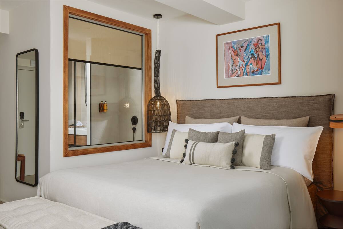 A bedroom with a large bed, a bedside table, a mirror, a hanging light fixture, and a framed artwork on the wall.