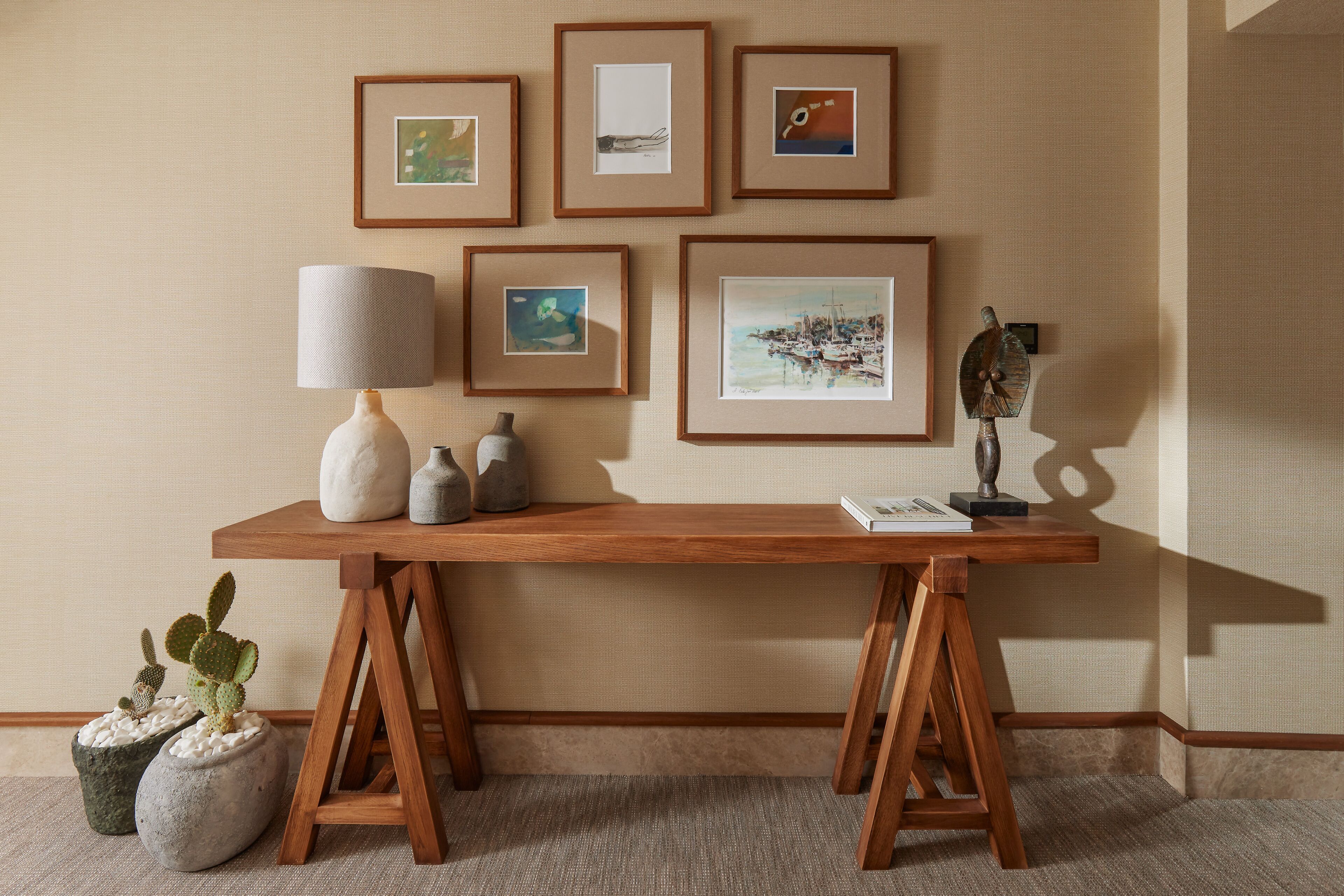 A wooden desk with a lamp, framed artwork, and potted plants.