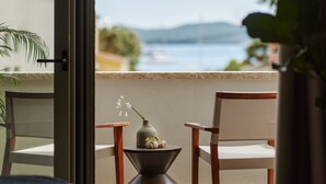 Un balcón con dos sillas, una mesita y un jarrón con flores. Se ve el mar y las montañas a través de la puerta abierta.