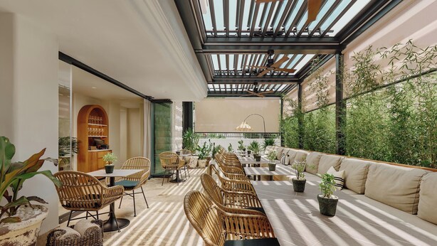 Un área de comedor al aire libre, moderna, con mobiliario de mimbre, una mesa larga y plantas en macetas.