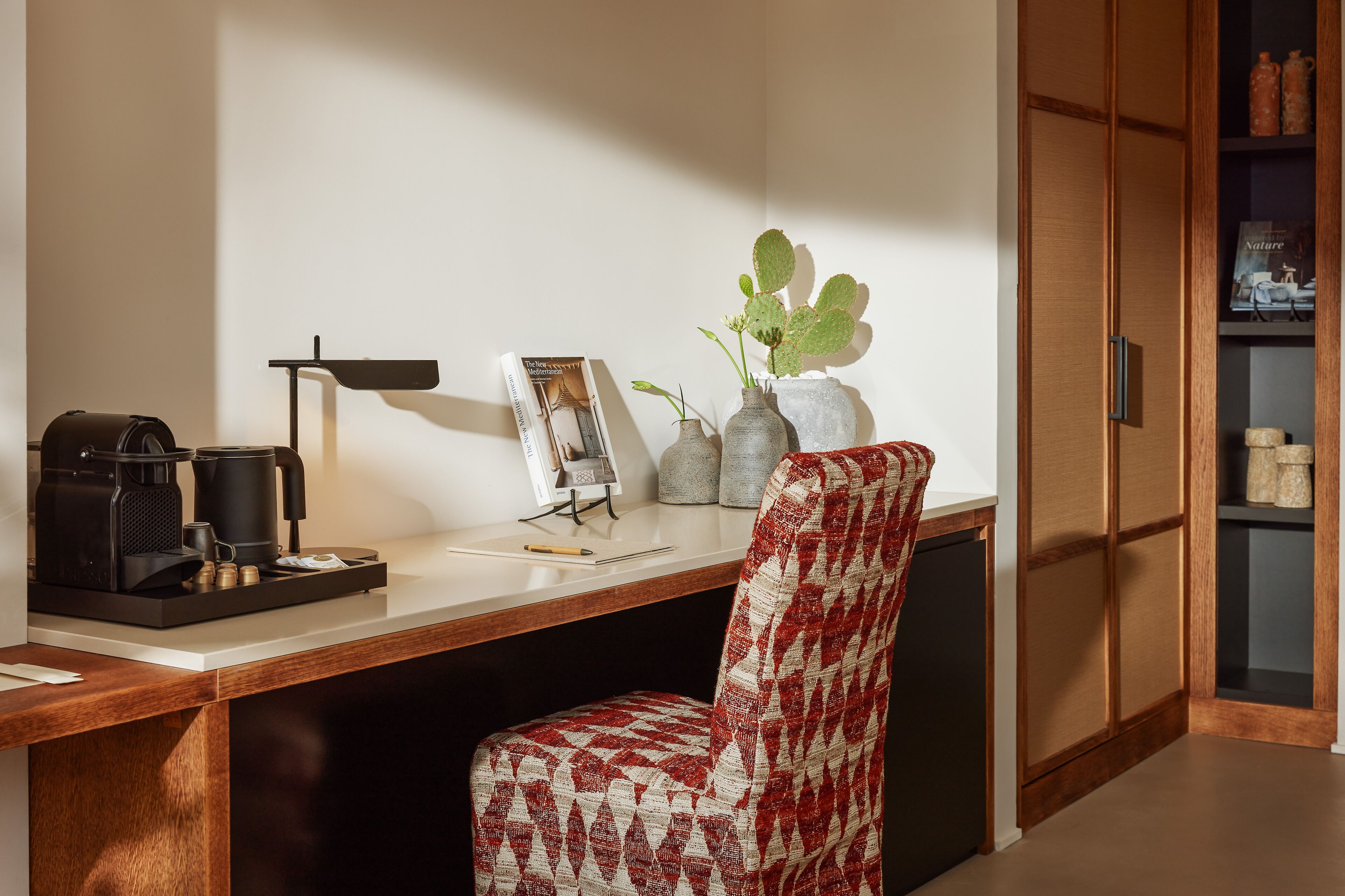 A modern kitchen with a wooden countertop, a coffee machine, a vase with a plant, and a bookshelf.