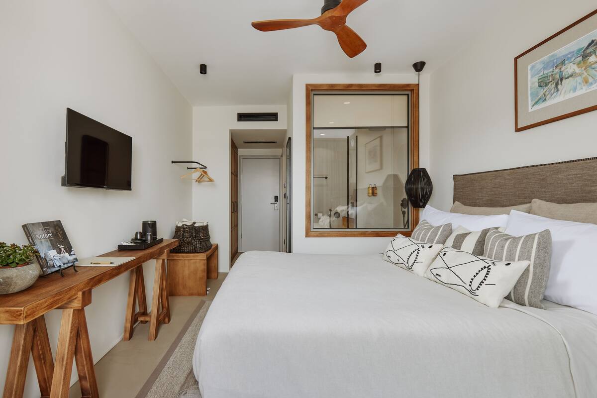 A modern bedroom with a large bed, a wooden desk, a flat-screen TV, and a ceiling fan.